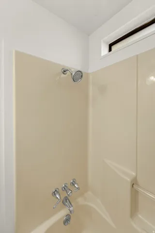 Bathtub with a cream-toned surround, chrome showerhead, and matching fixtures