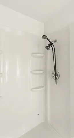White shower surround with built-in corner shelving and a dual shower head fixture