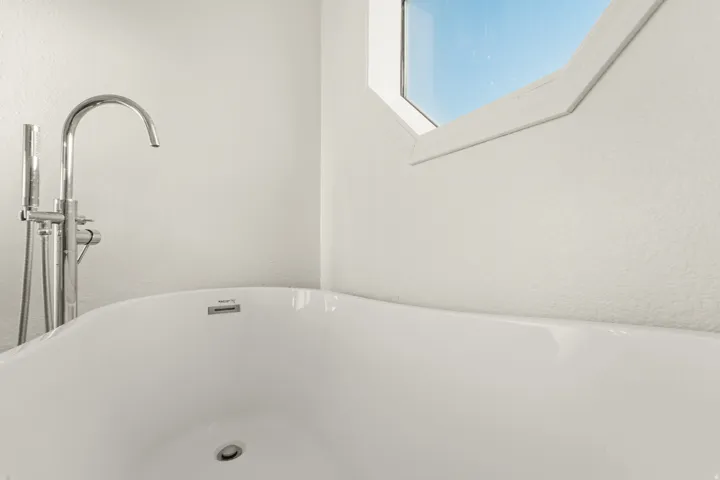 Freestanding soaking tub with chrome floor-mounted filler faucet and handheld sprayer