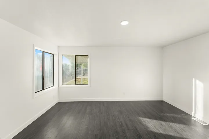 Spacious room featuring dark wood-finish flooring, white baseboards, and two large windows with white trim