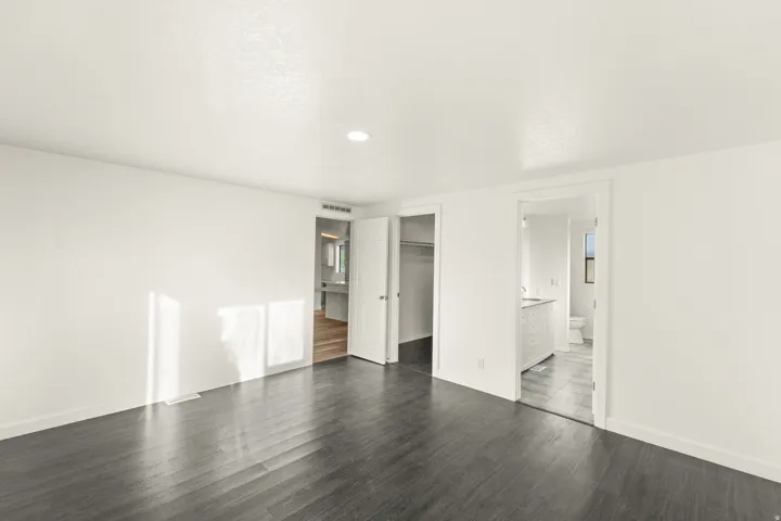 Spacious room featuring dark wood-finish flooring and crisp white walls