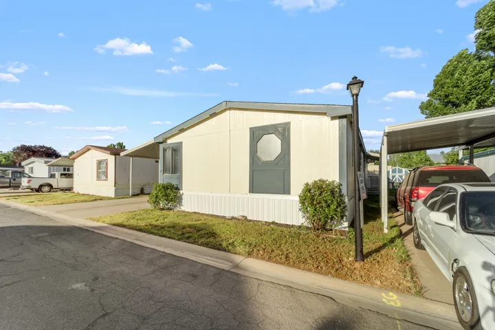 Exterior featuring light-colored siding, a covered carport, a street lamp, and front landscaping