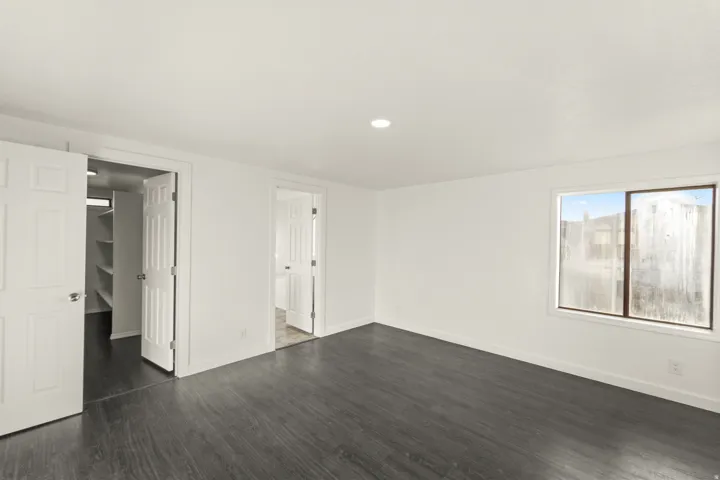 Spacious room featuring dark wood-finish flooring, recessed lighting, and a window with white trim