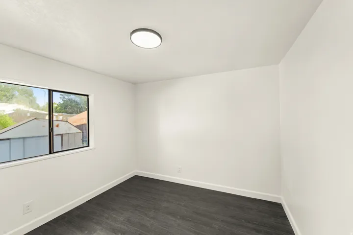 Spacious room featuring wood-finish flooring, crisp white walls, and a large window