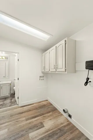 Functional utility space featuring wood-finish flooring, white wall-mounted cabinetry, and a rectangular ceiling light fixture