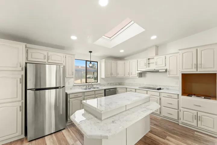 Kitchen featuring a central island with a multi-level countertop, light-toned cabinetry, stainless steel appliances, a skylight, and wood-finish flooring