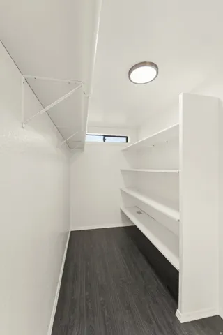 Walk-in storage area featuring multiple white shelving units, wood-finish flooring, a recessed ceiling light, and a horizontal window