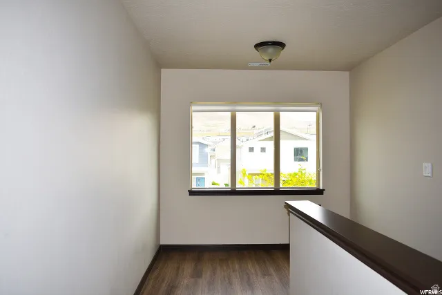 Windowed interior space with wood-finish flooring, a flush-mount ceiling light fixture, a dark wood-finish window sill, and a dark wood-finish railing