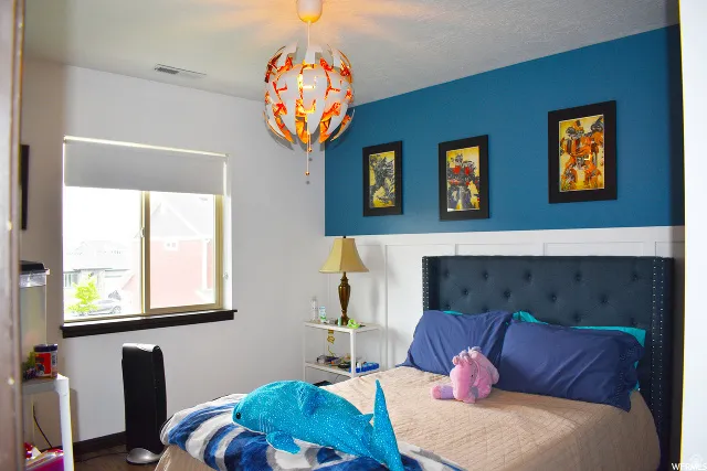 Room featuring wood-finish flooring, a contemporary ceiling light fixture, a window with a roller shade, a decorative accent wall, and wainscoting