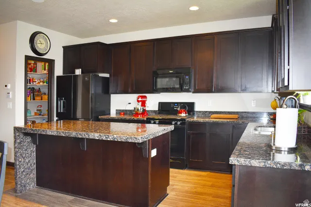 Kitchen featuring dark wood-finish cabinetry, speckled countertops, and wood-finish flooring