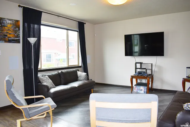 Living area featuring a large window with dark drapes, wood-finish flooring, and a mounted wall display