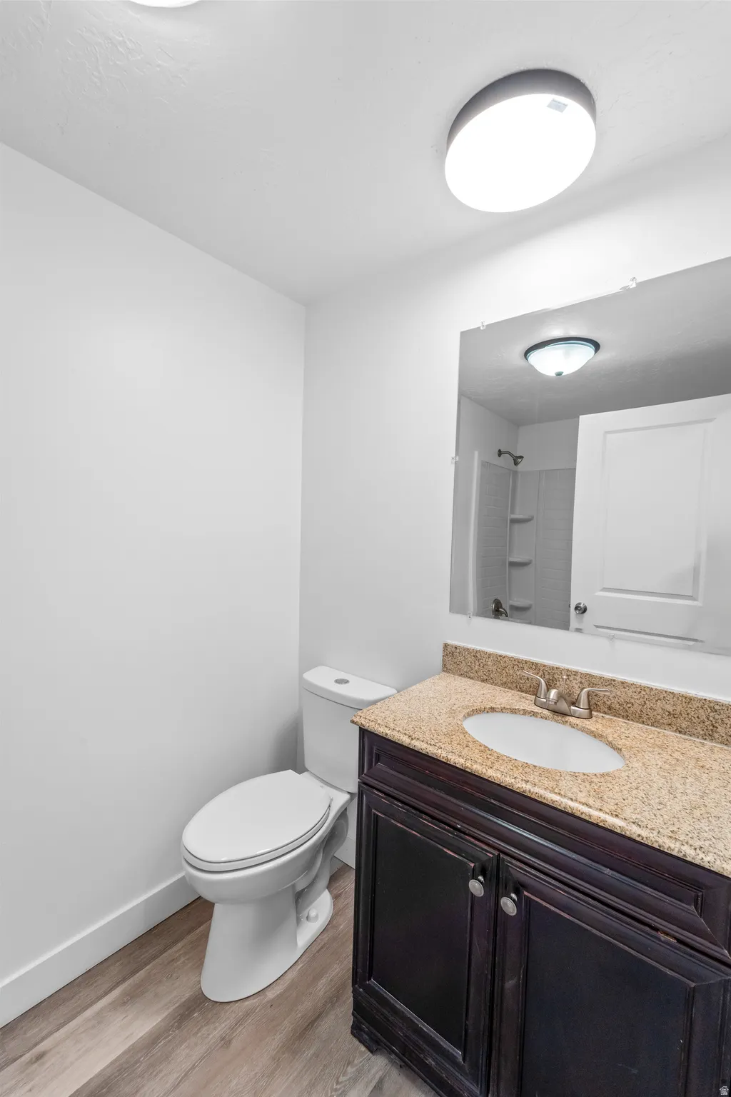 Bathroom featuring a dark wood-finish vanity with a light-toned stone countertop, an undermount sink, and a framed mirror