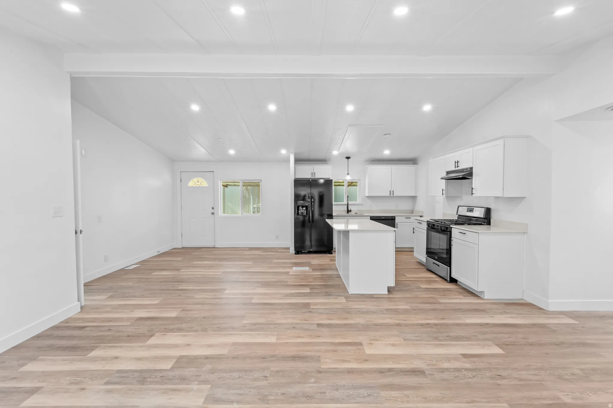 Open-concept living area with wood-finish flooring, recessed lighting, and a white kitchen featuring a central island, white cabinetry, and black appliances