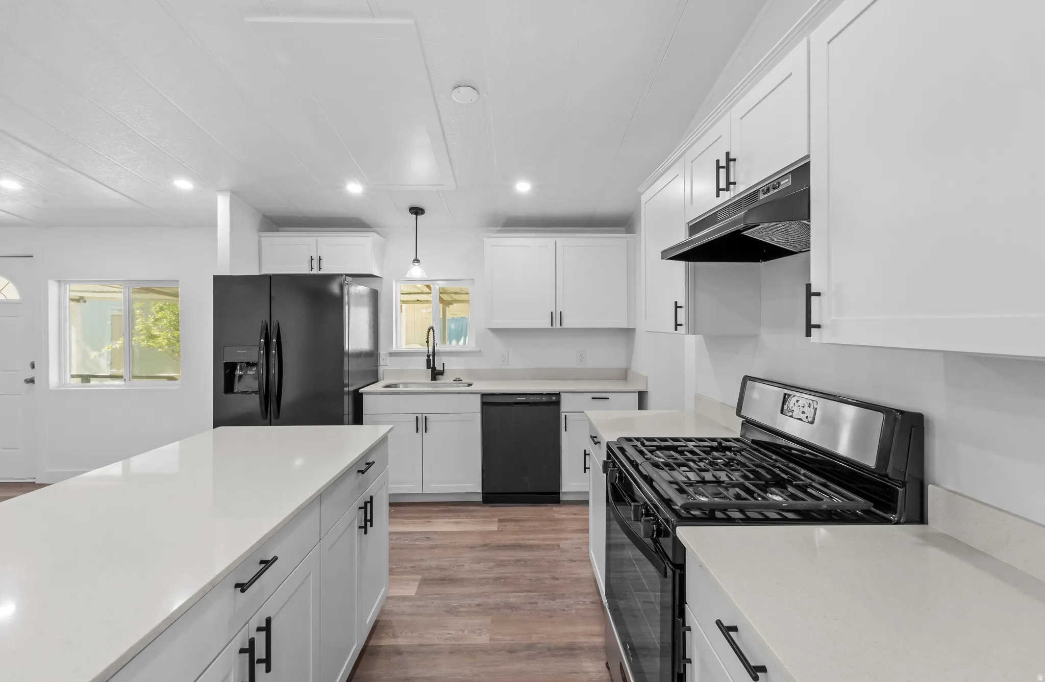 Modern kitchen featuring white shaker cabinetry, light-toned countertops, wood-finish flooring, a central island, and black appliances including a gas range