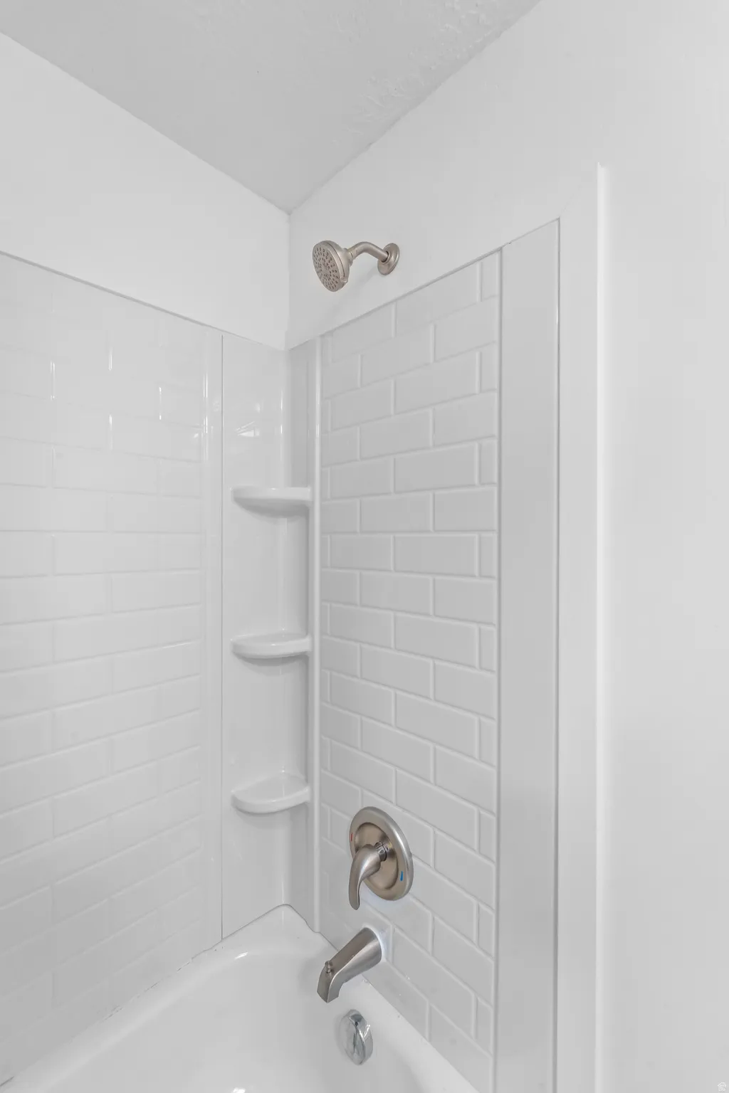 Bathtub with white subway tile surround, integrated shelving, and brushed nickel fixtures