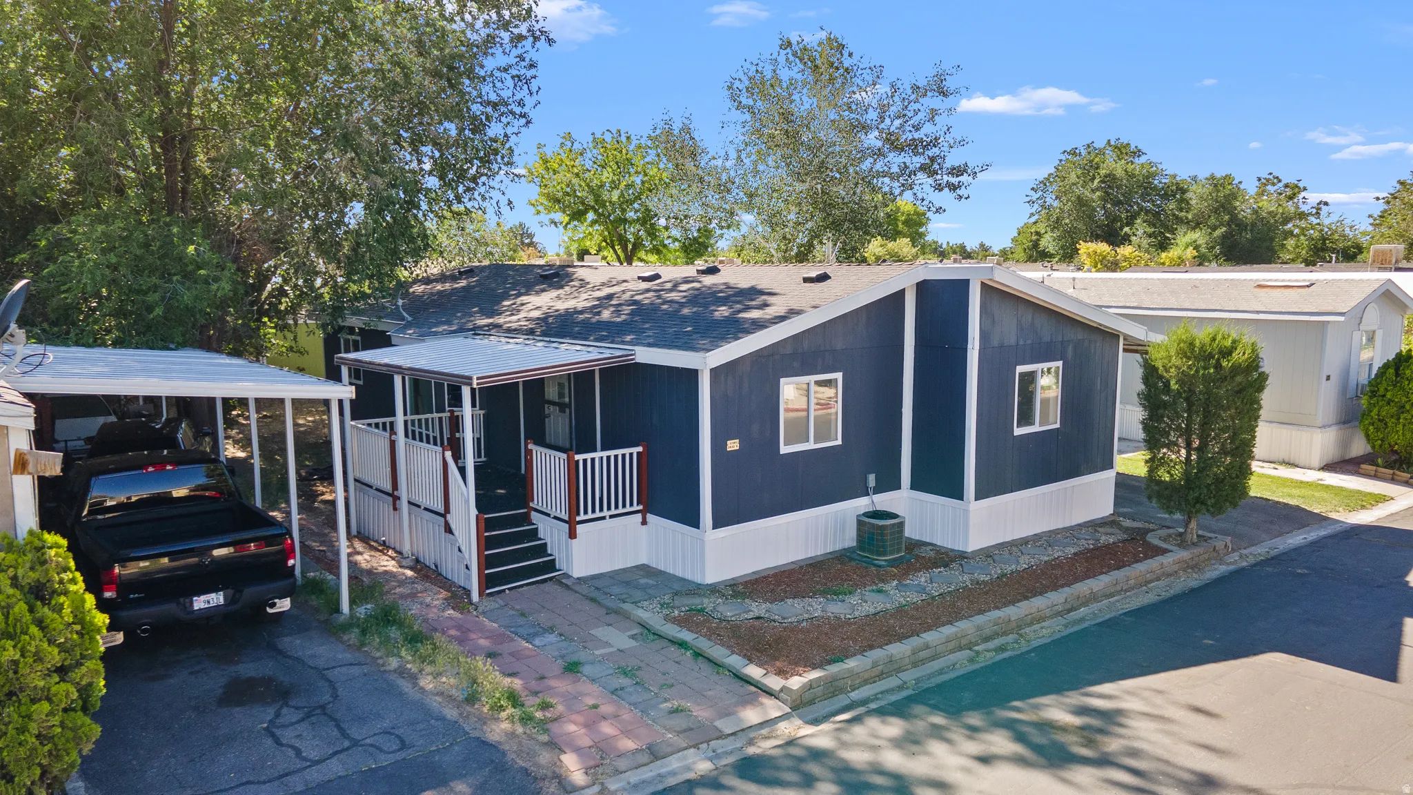 Single-story residence featuring dark blue siding with white trim, a covered front porch with white railings and dark wood accents, and a dedicated carport
