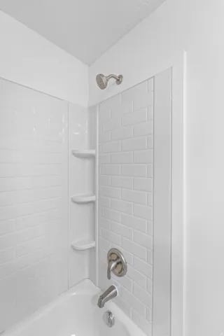Bathtub with white subway tile surround, integrated shelving, and brushed nickel fixtures