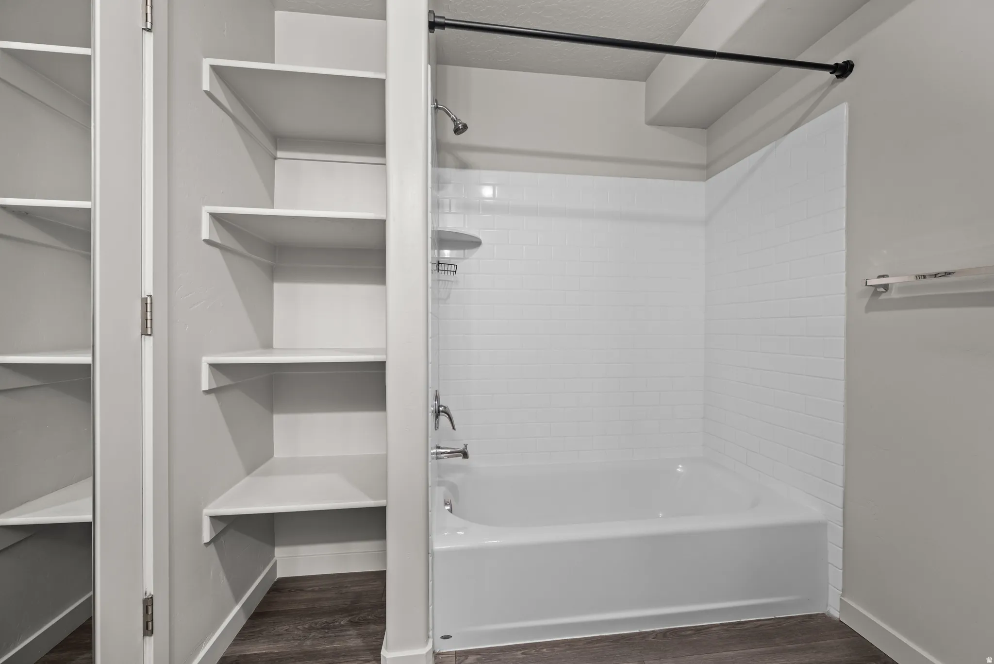 Built-in shelving and tub/shower combination with subway tile surround, chrome fixtures, and a black shower rod