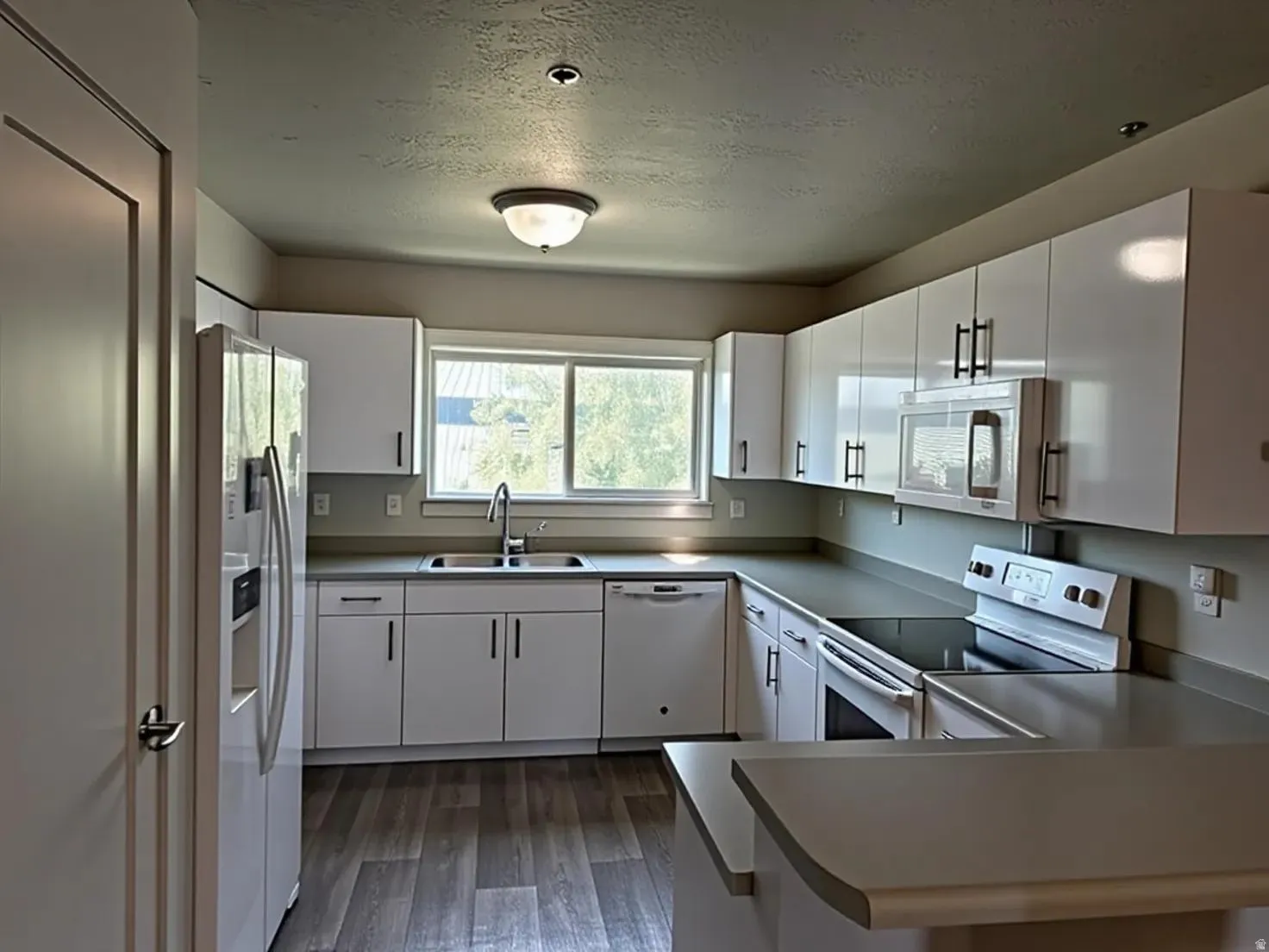 Modern kitchen featuring white cabinetry with dark hardware, stone-look countertops, and wood-finish flooring