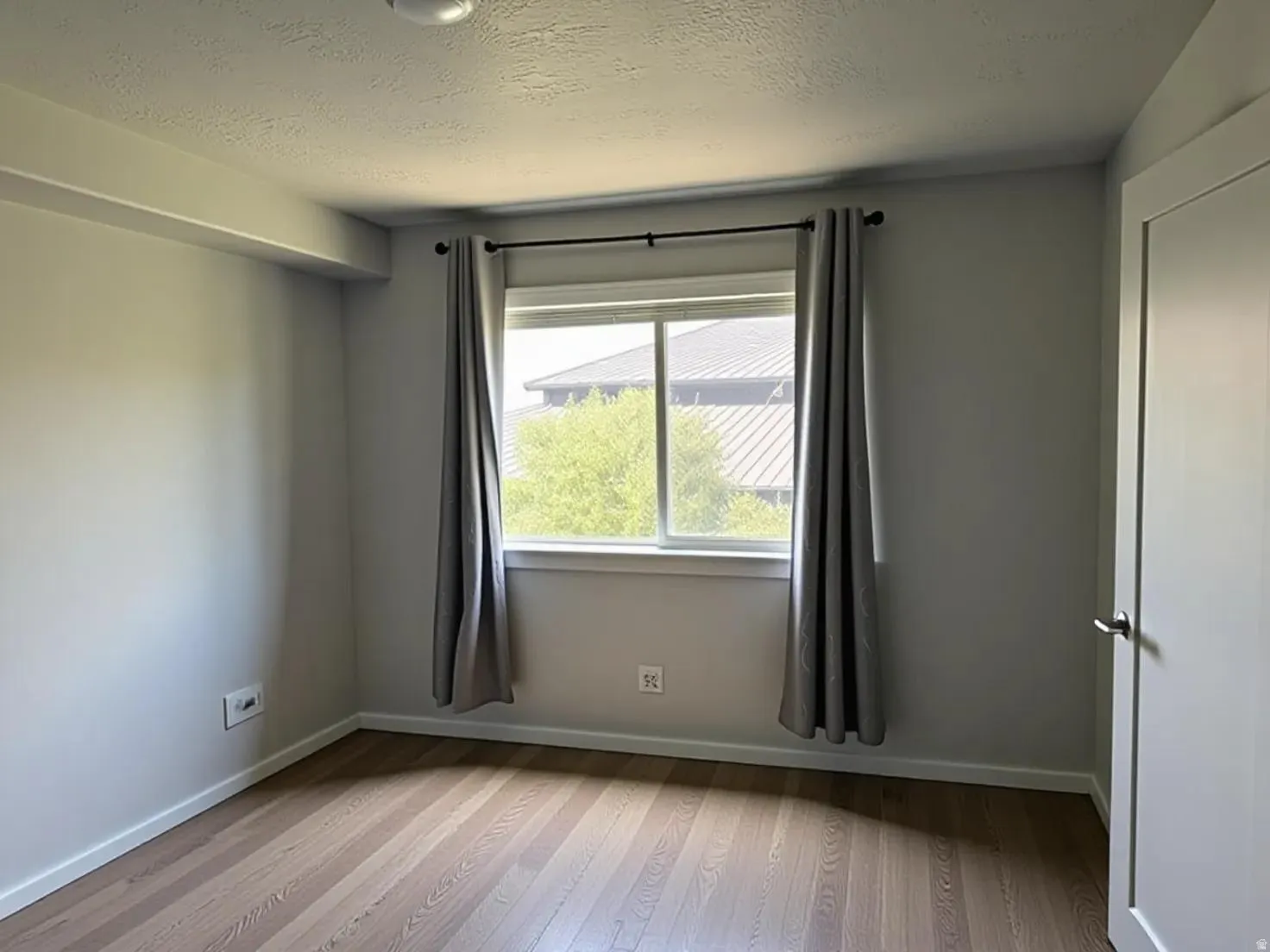 Room featuring wood-finish flooring, a window with a black curtain rod, and a solid-core door with a brushed nickel handle