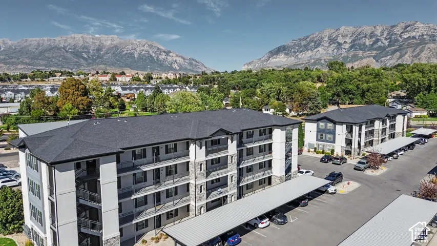 Multi-story exterior featuring stone veneer accents, neutral stucco siding, asphalt shingle roofing, private balconies, and covered parking structures against a mountain backdrop