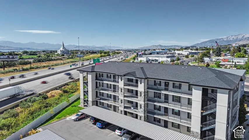 Multi-story building with stone-veneer accents, metal-roofed covered parking, private balconies, and mountain backdrops