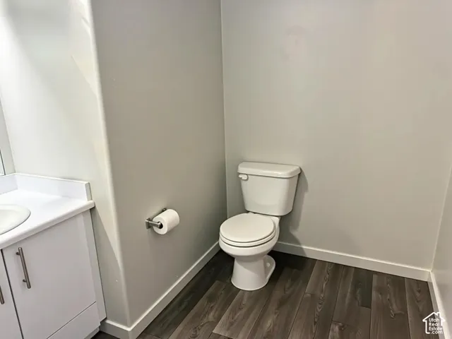 Compact bathroom featuring a white toilet, contemporary white vanity with integrated sink, brushed nickel hardware, wood-finish flooring, and crisp white baseboards