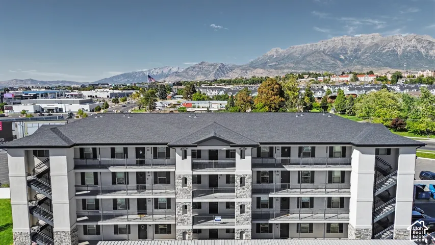 Multi-story building featuring a stone-veneer facade, dark shingle roof, exterior stairwells, and multi-level balconies, set against a mountain backdrop