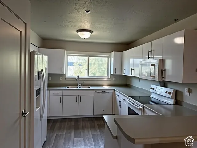 Modern kitchen featuring white cabinetry with dark hardware, stone-look countertops, and wood-finish flooring