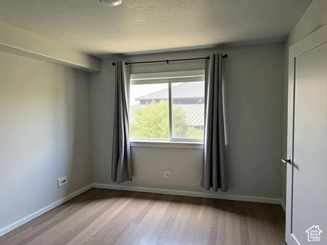 Room featuring wood-finish flooring, a window with a black curtain rod, and a solid-core door with a brushed nickel handle