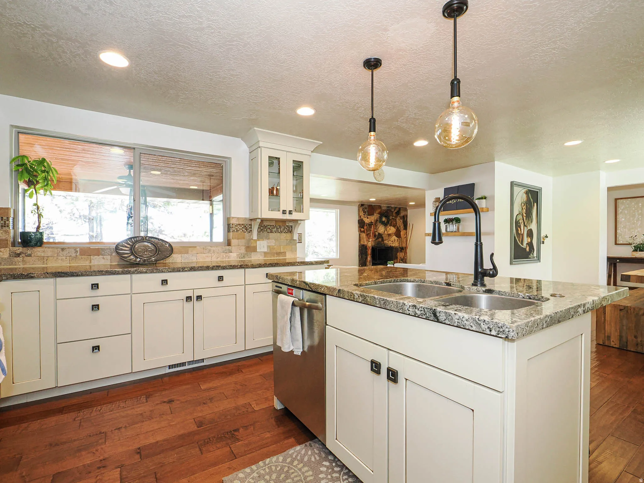 Kitchen featuring a central island with a double sink and dark-finish faucet, under-cabinet storage, stainless steel dishwasher, wood-finish flooring, and recessed lighting