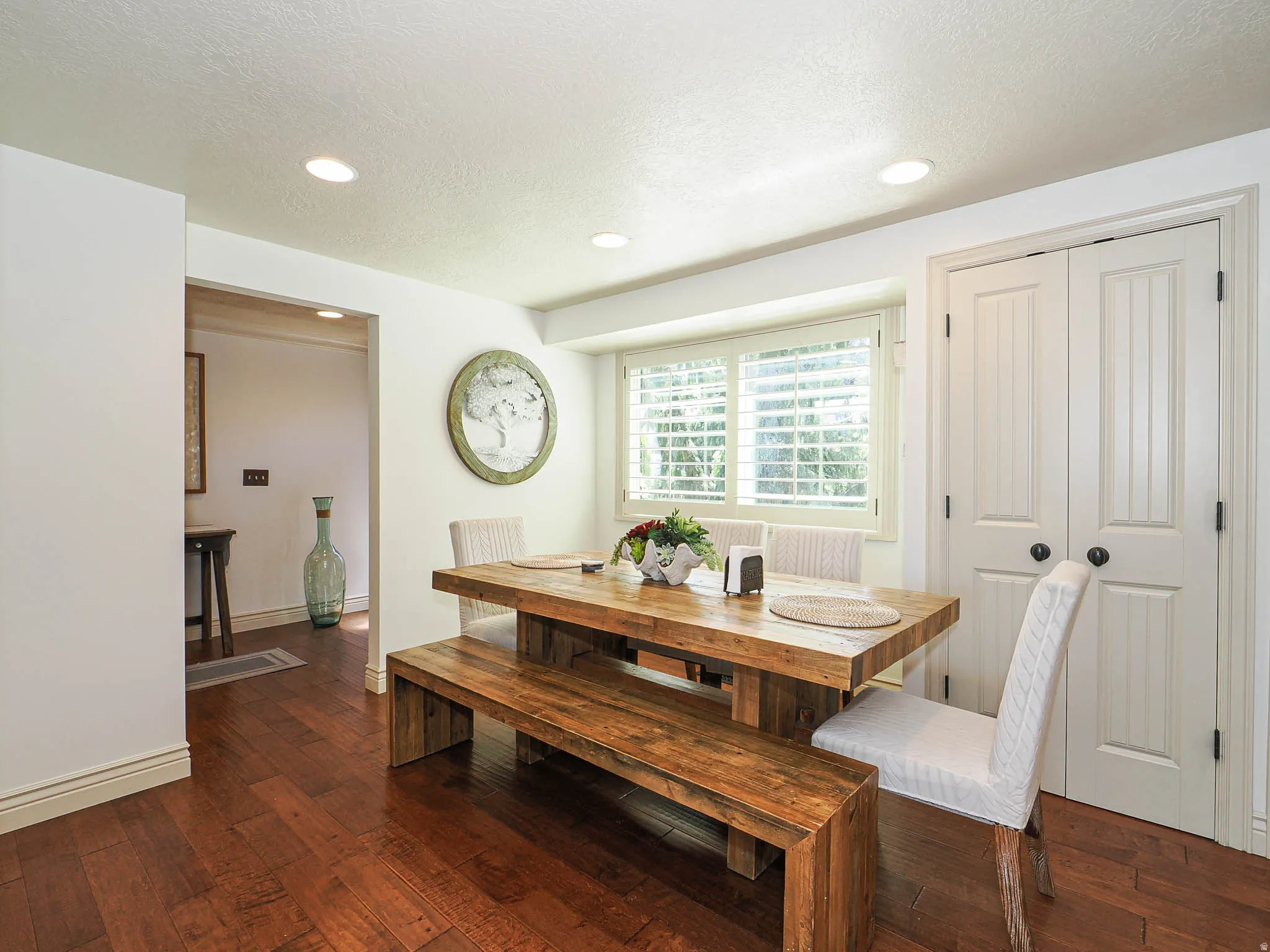 Dining area featuring rich wood-finish flooring, recessed lighting, and a white plantation-shutter window