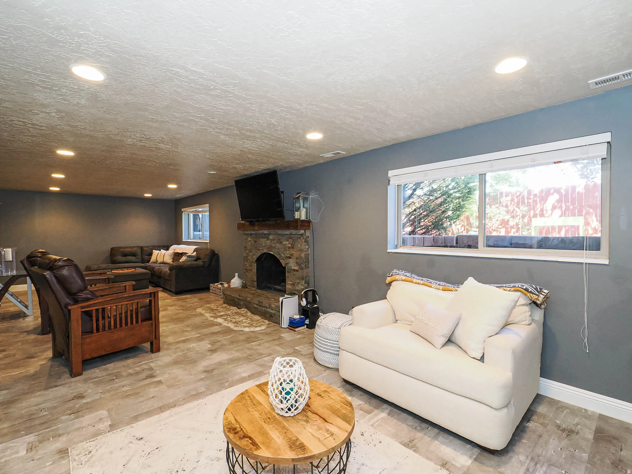 Spacious room featuring wood-finish flooring, recessed lighting, and a stone-clad fireplace with a wood mantel