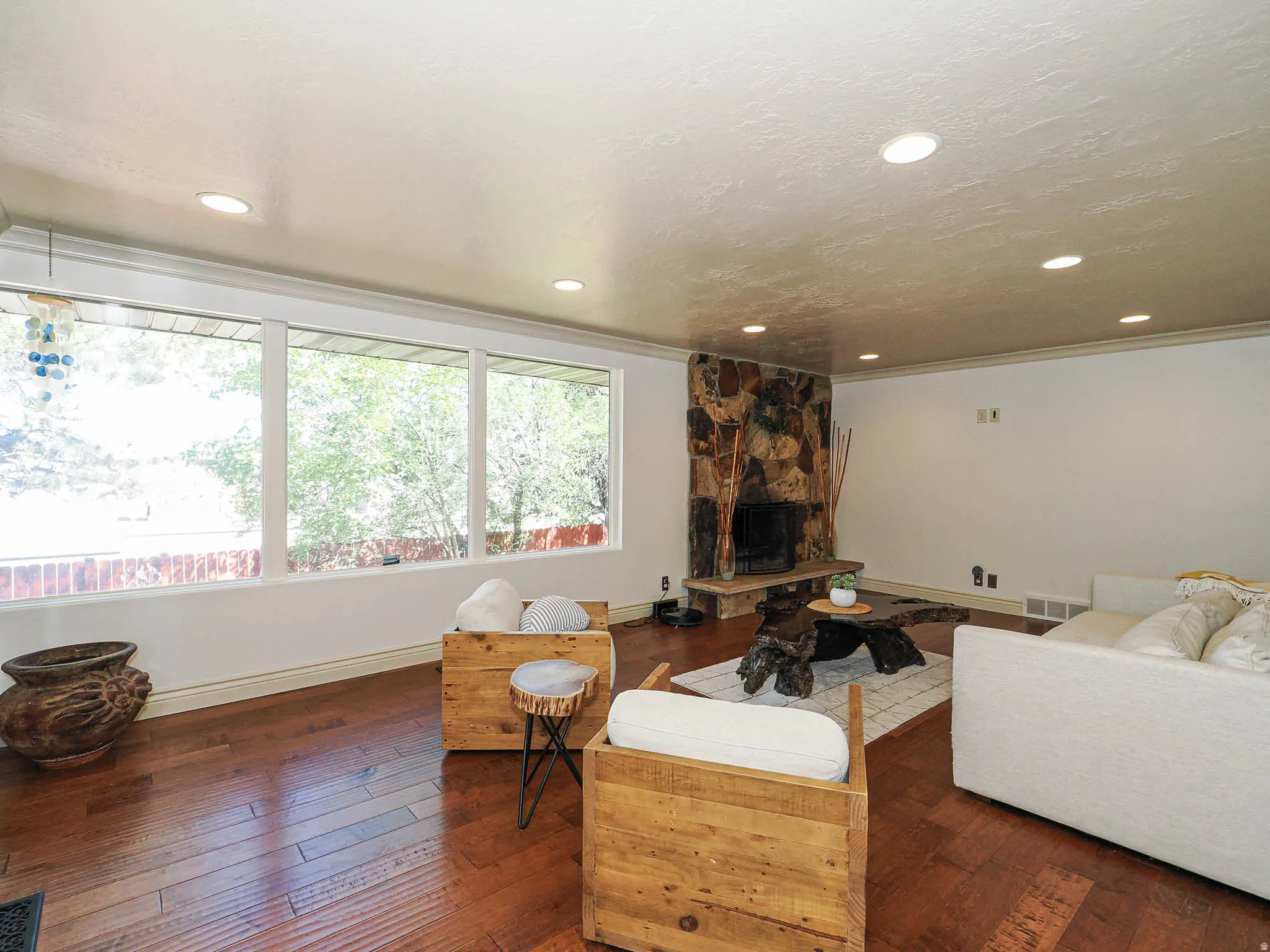 Living space featuring expansive windows, wood-finish flooring, a stone-clad fireplace with a hearth, recessed lighting, and white wall finishes