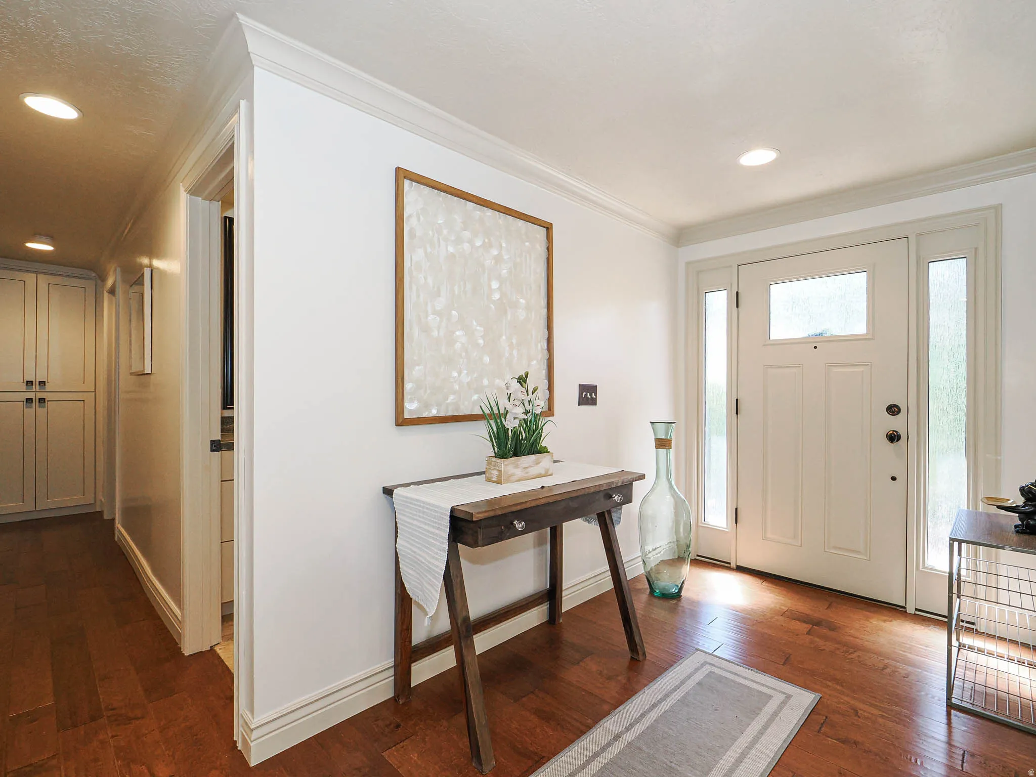 Entryway featuring a paneled door with sidelight windows, rich wood-finish flooring, recessed lighting, crown molding, and built-in cabinetry in the adjacent hallway