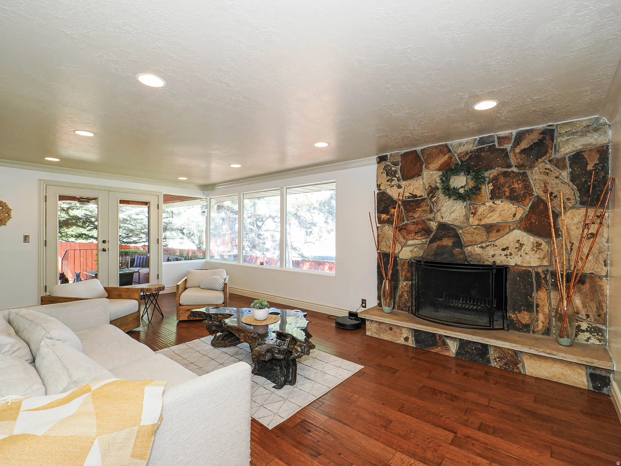 Living area featuring a floor-to-ceiling stone fireplace, rich wood-finish flooring, recessed lighting, and expansive windows