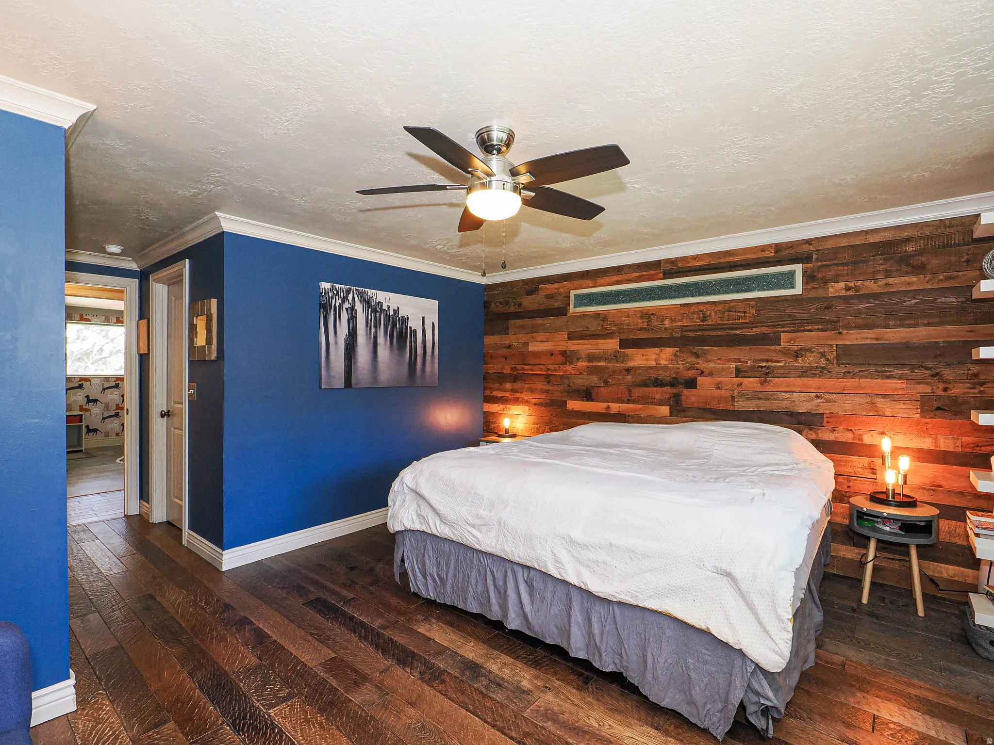 Bedroom featuring wood-finish flooring, a wood-paneled accent wall, and a ceiling fan with integrated lighting