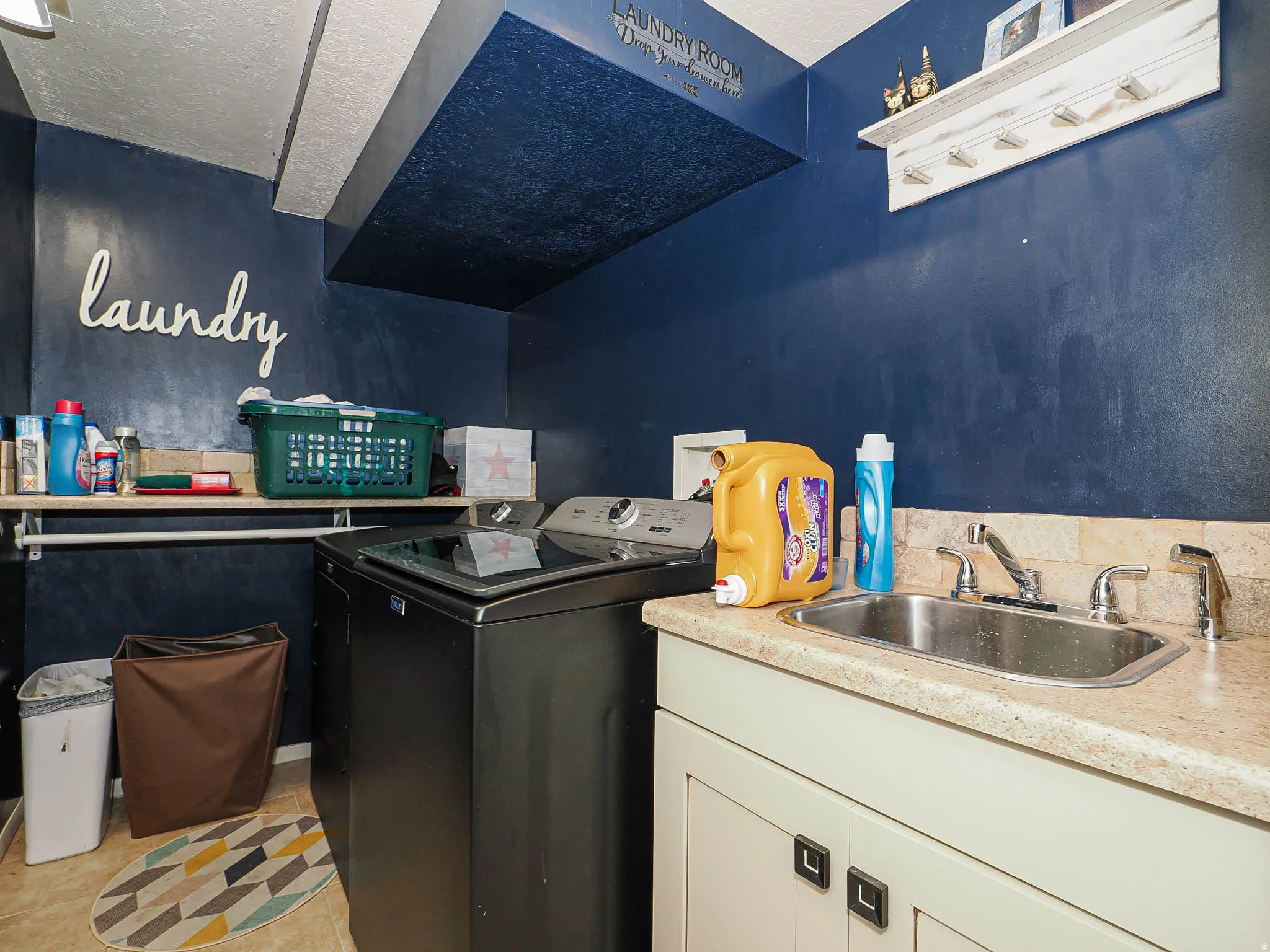 Laundry room featuring a built-in utility sink with a chrome faucet, light-toned countertop, and cream-colored cabinetry