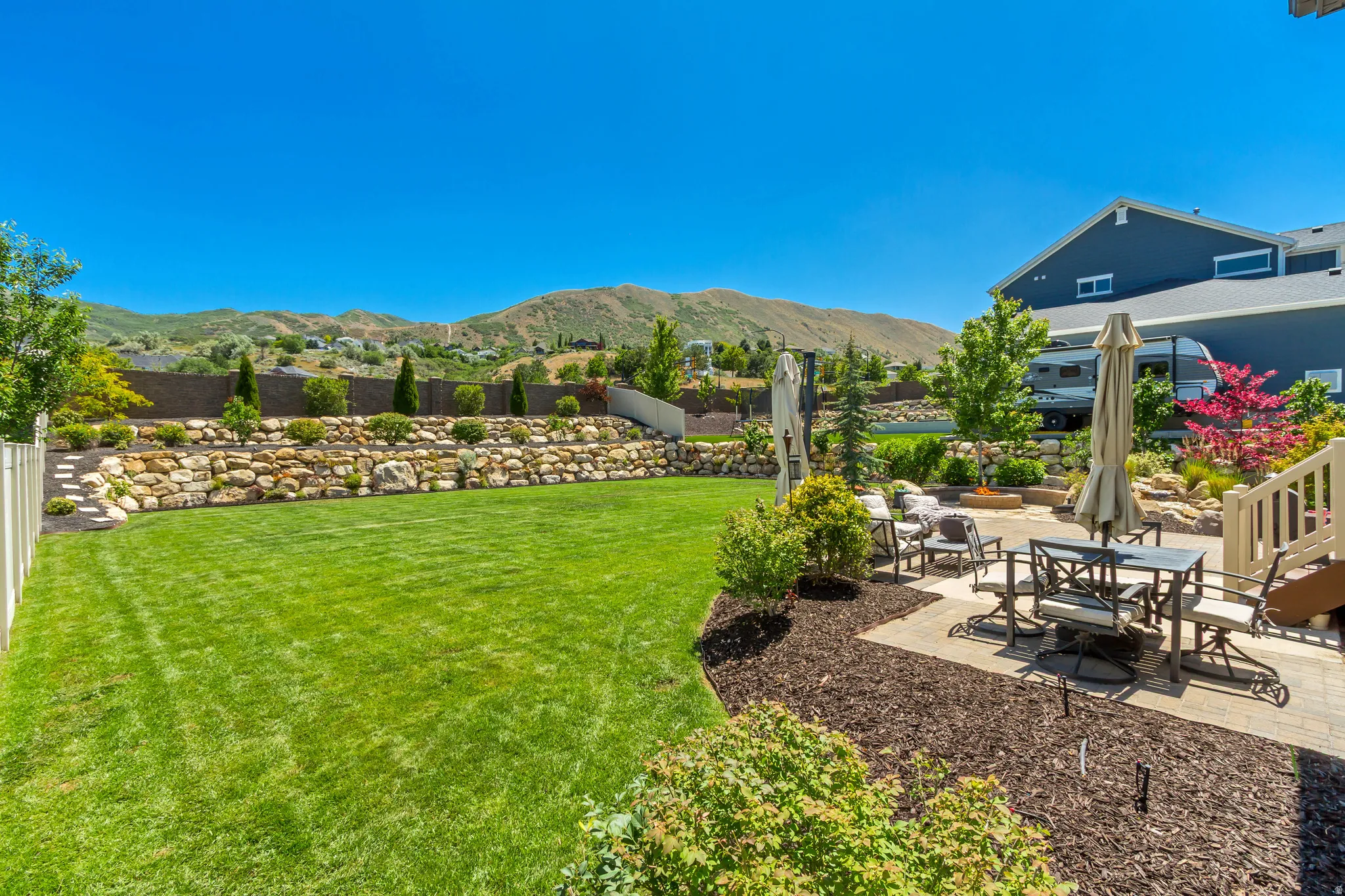 Expansive backyard featuring a manicured lawn, a multi-tiered rock retaining wall, and mature landscaping