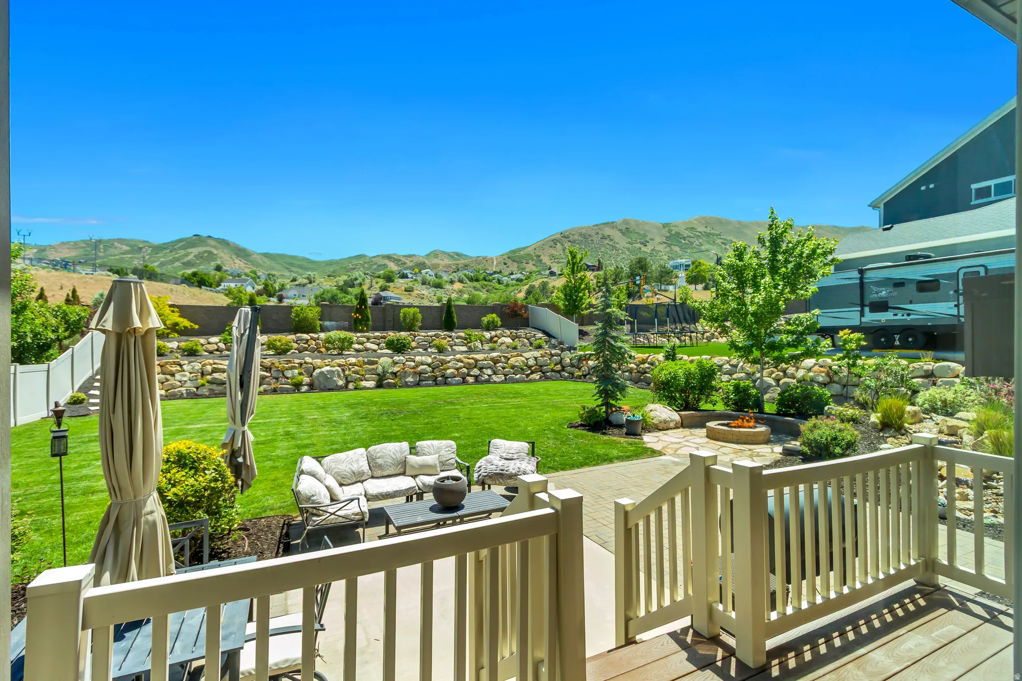 Expansive backyard featuring a manicured lawn, a flagstone patio with a built-in fire pit, and tiered landscaping with natural rock retaining walls