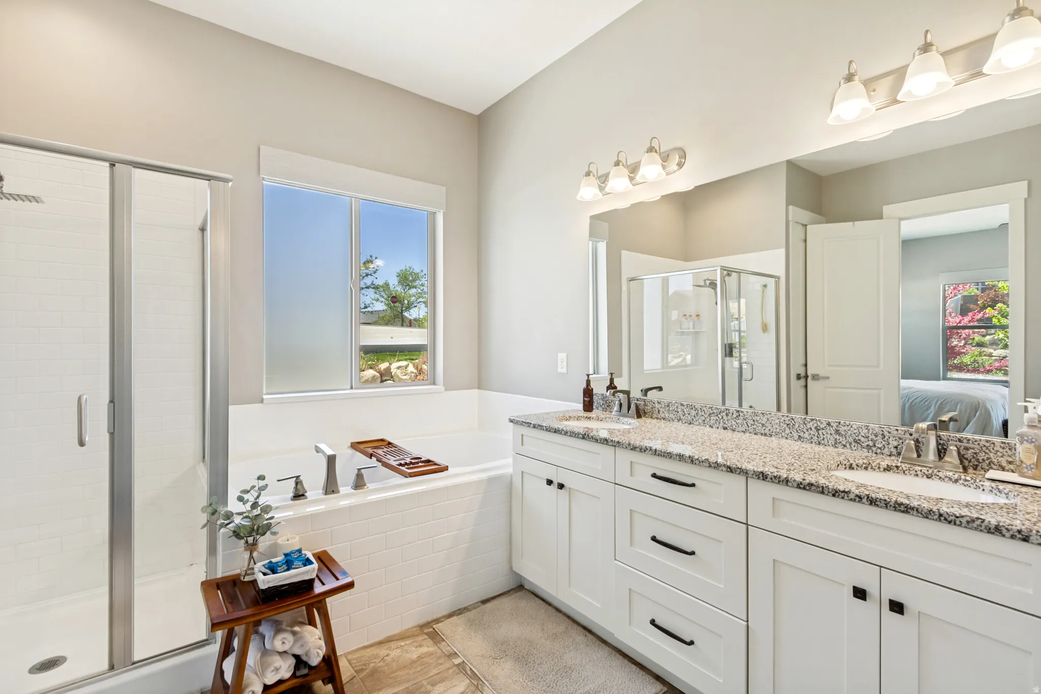 Bathroom featuring a built-in tub with tile surround, a separate glass-enclosed shower, dual vanity with granite countertop, and tile flooring