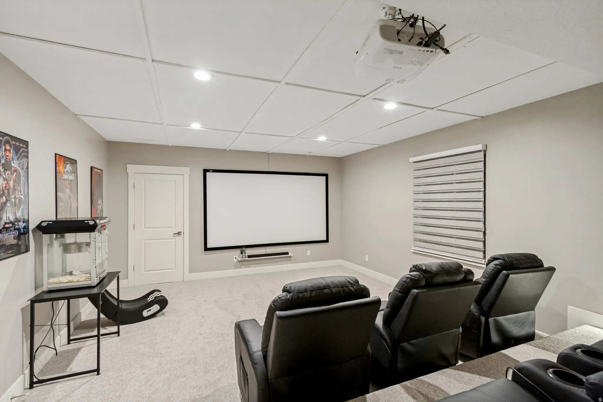 Dedicated media room featuring a large projector screen, ceiling-mounted projector, recessed lighting, and light-filtering window treatments