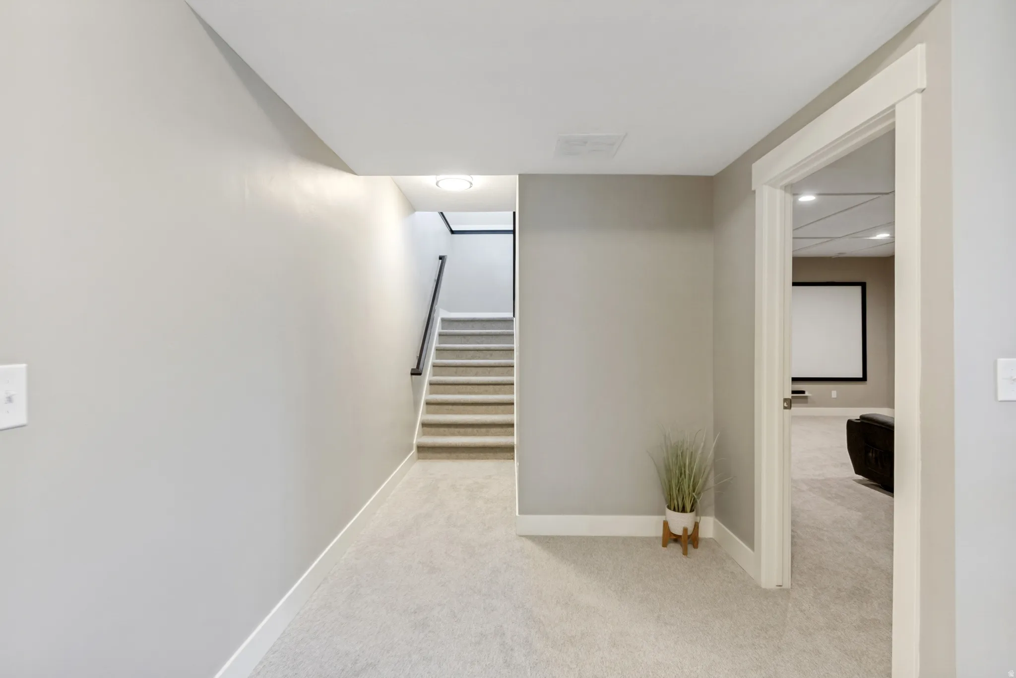 Carpeted hallway with light gray walls, white baseboards, and a staircase featuring a black handrail