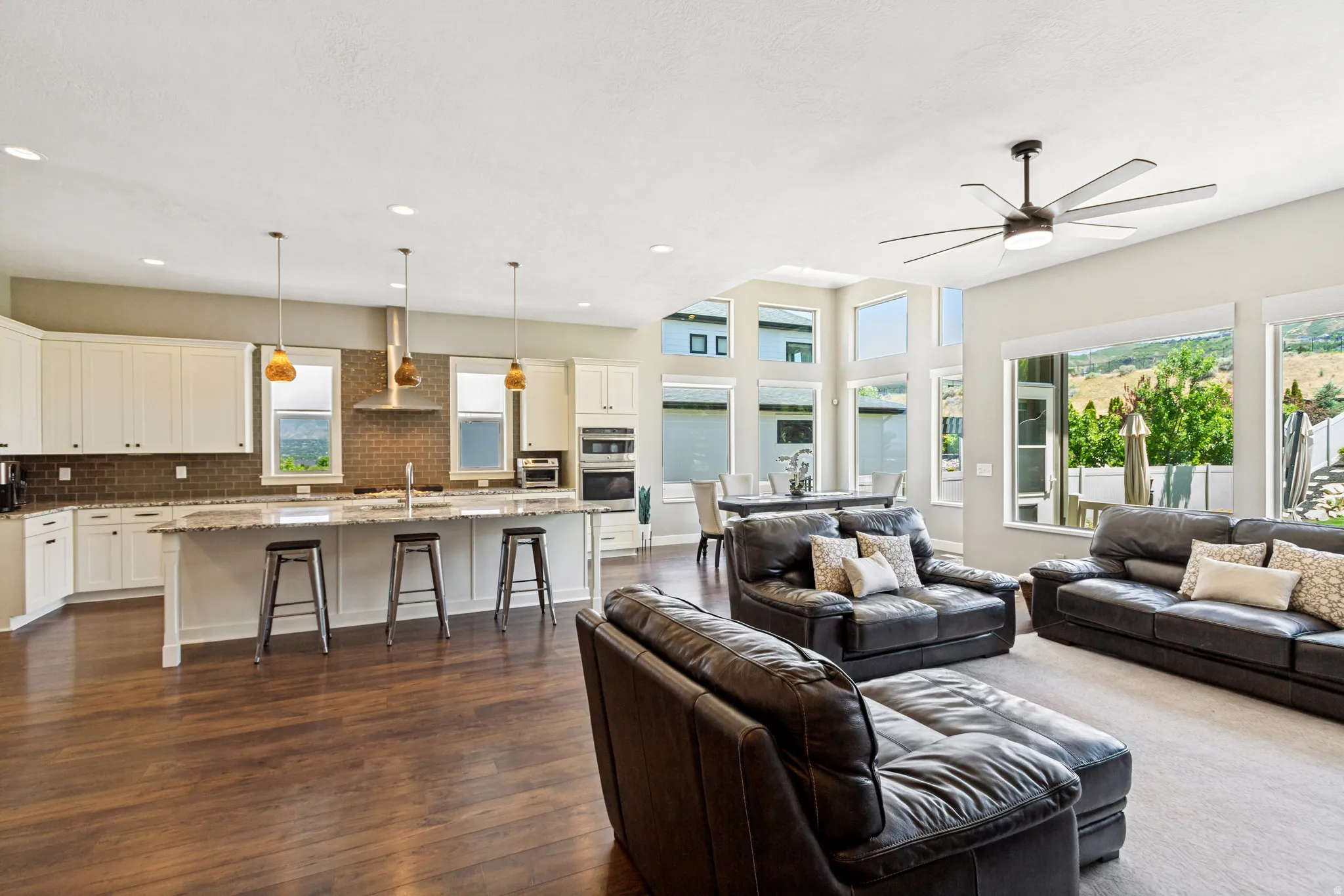 Open-concept living space featuring wood-finish flooring, a kitchen island with seating, white cabinetry, a tiled backsplash, and recessed lighting