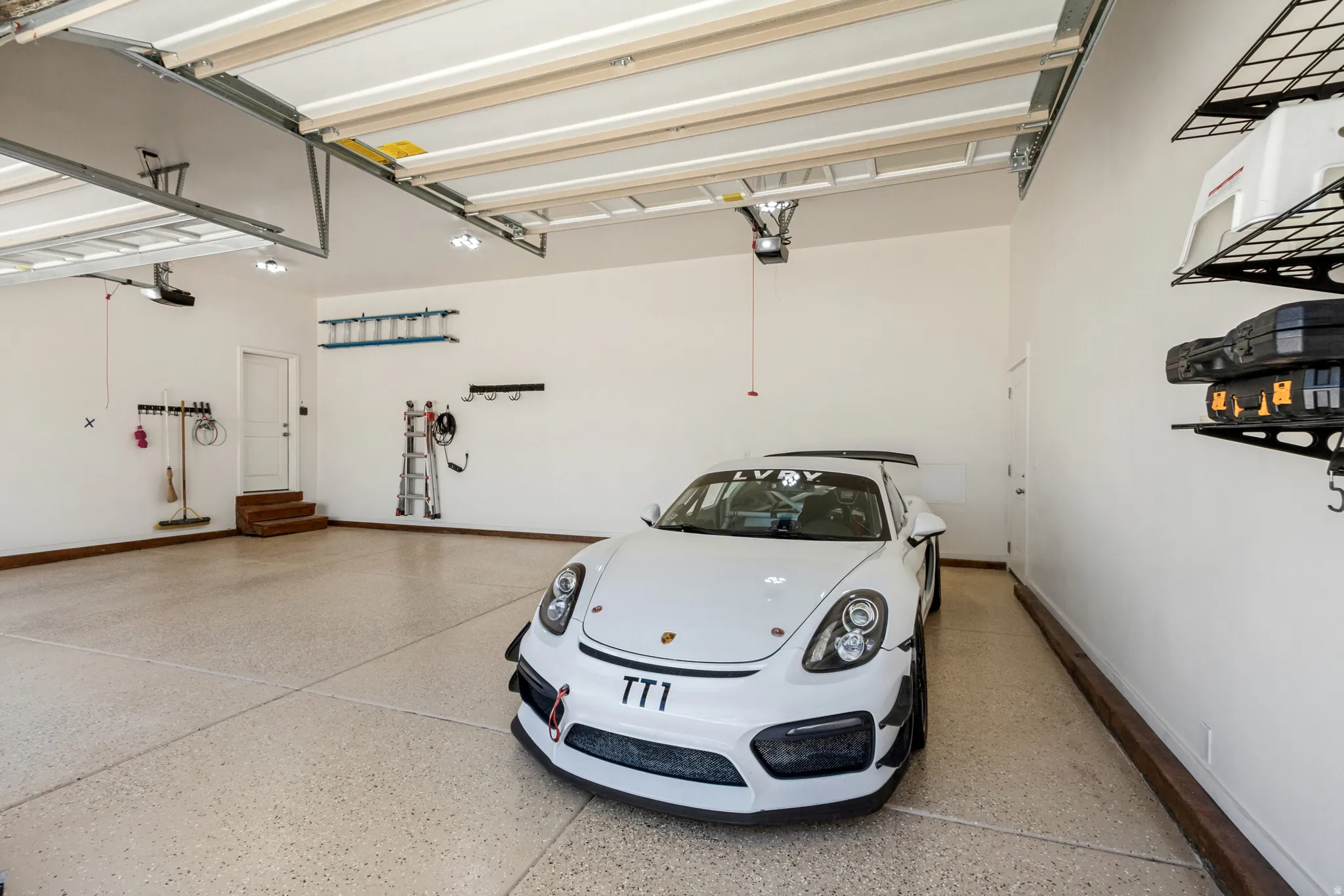 Spacious garage featuring a light-colored epoxy floor, overhead lighting, and wall-mounted storage shelves