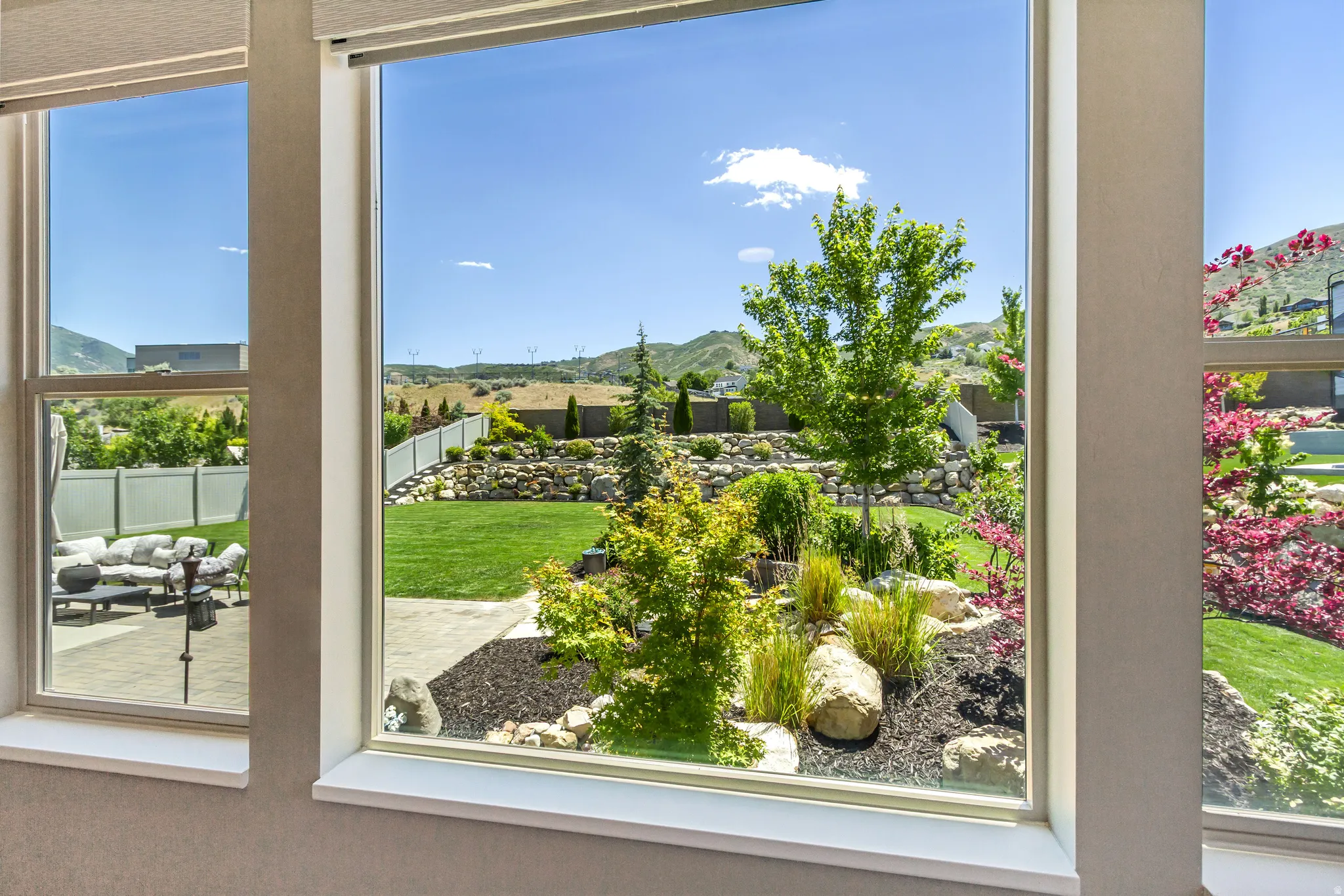 Expansive backyard featuring a tiered landscape, a manicured lawn, mature trees, and vibrant plantings