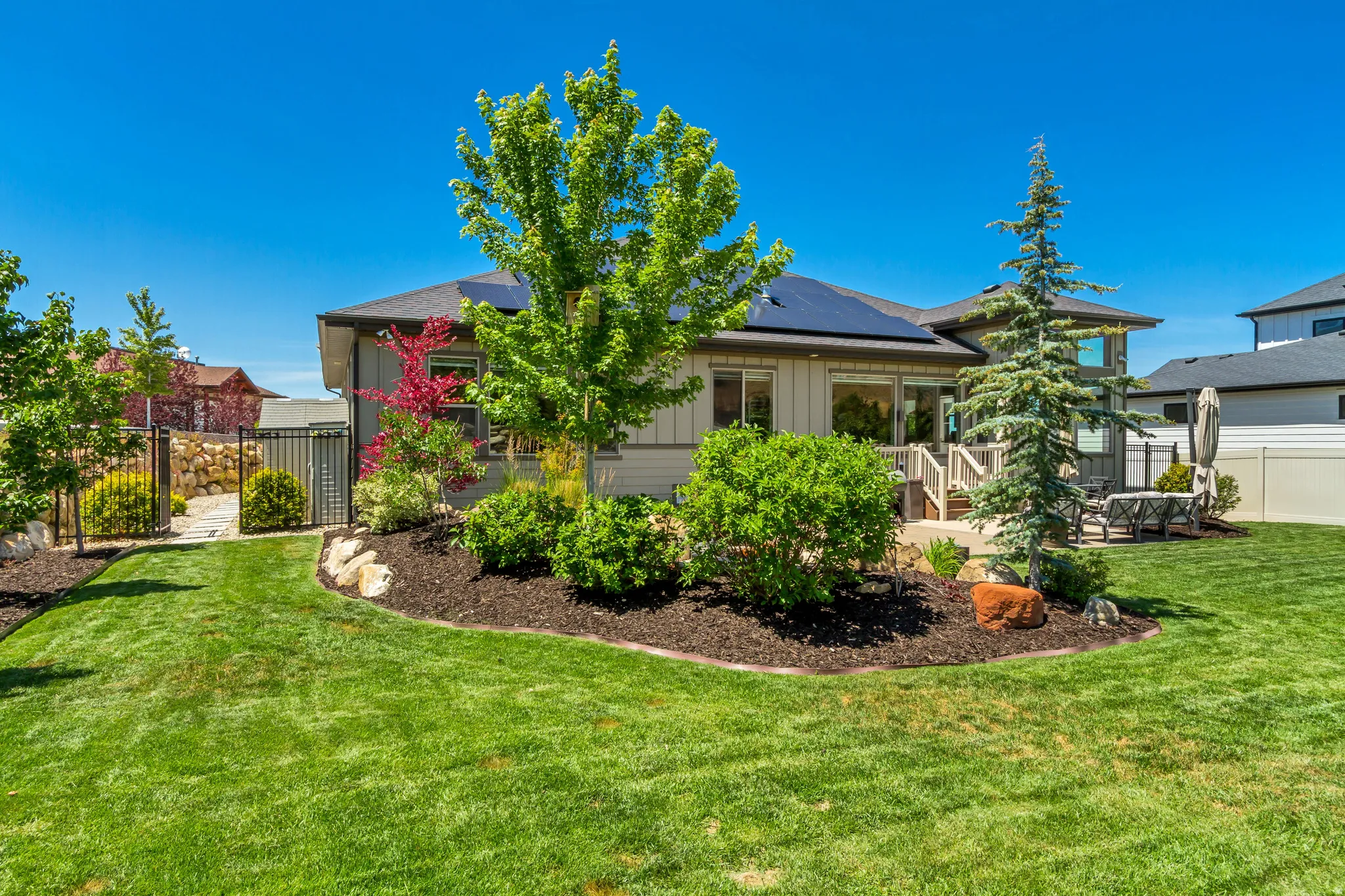 Expansive green lawn with established landscaping beds, a stone pathway, and a patio area