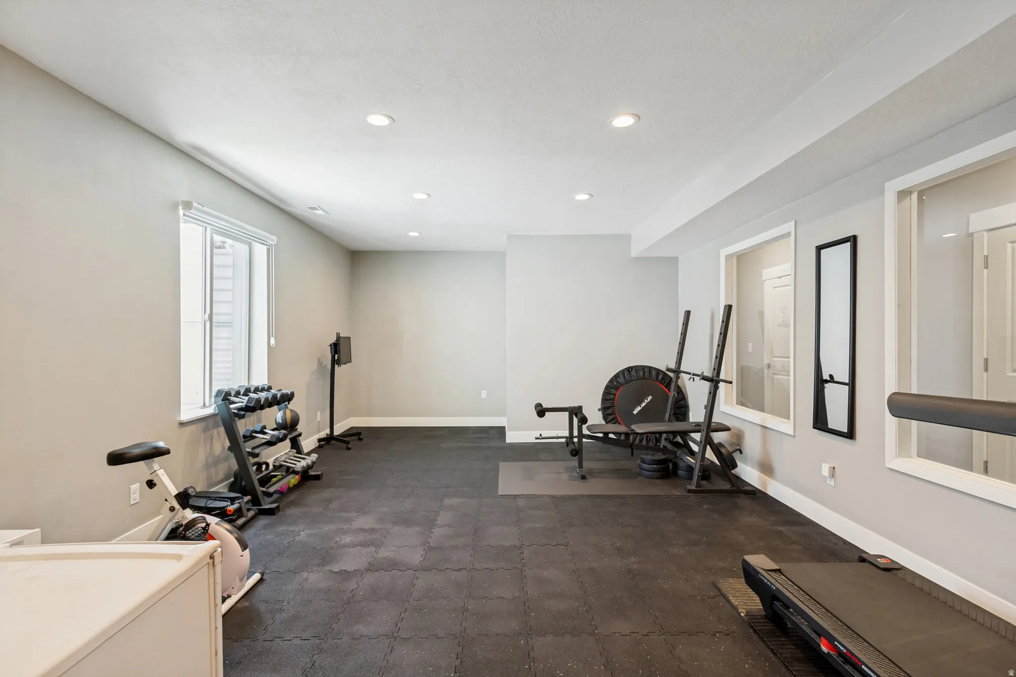 Spacious room featuring recessed lighting, a window with blinds, and durable black rubber flooring