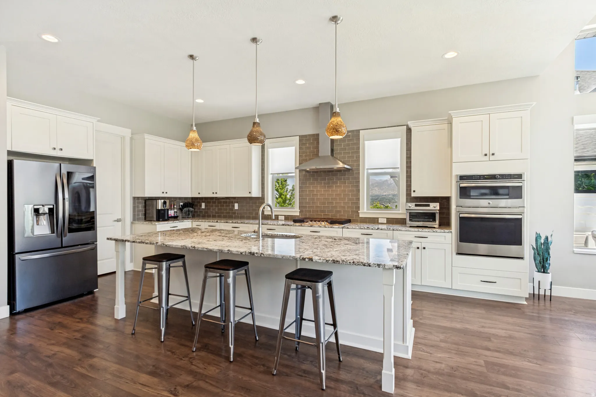 Spacious kitchen featuring an expansive center island with seating, wood-finish flooring, white cabinetry, integrated stainless steel appliances, and a tiled backsplash