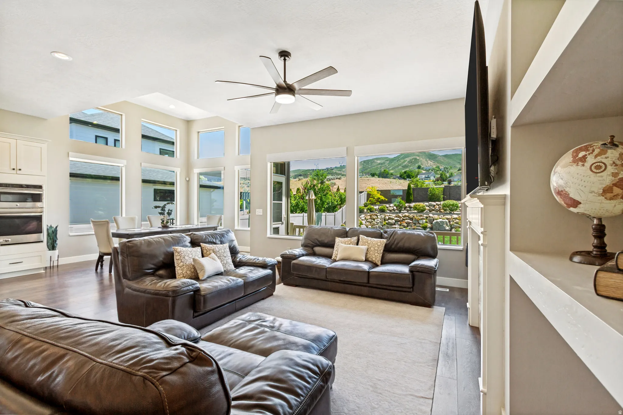 Open-concept living area featuring a vaulted ceiling with a contemporary ceiling fan, wood-finish flooring, and a stone-clad exterior visible through large windows